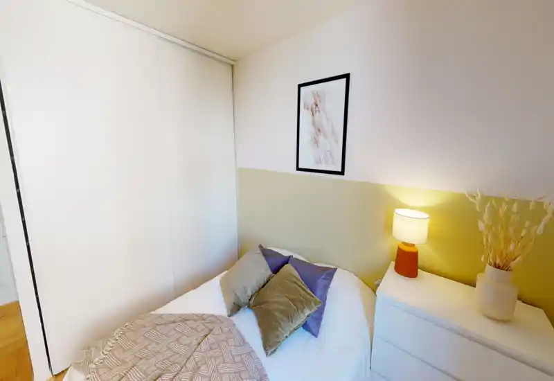 Bright, stylish bedroom view with a neatly made bed, decorative pillows and a warm bedside lamp on a white dresser; calm neutral tones and minimalist wall art create a cozy atmosphere.