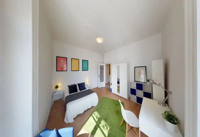 Bright, modern bedroom with a double bed, bedside tables and warm lamps. Large wardrobe, desk area and a green rug create a functional, well-styled living space ideal for rental photos.