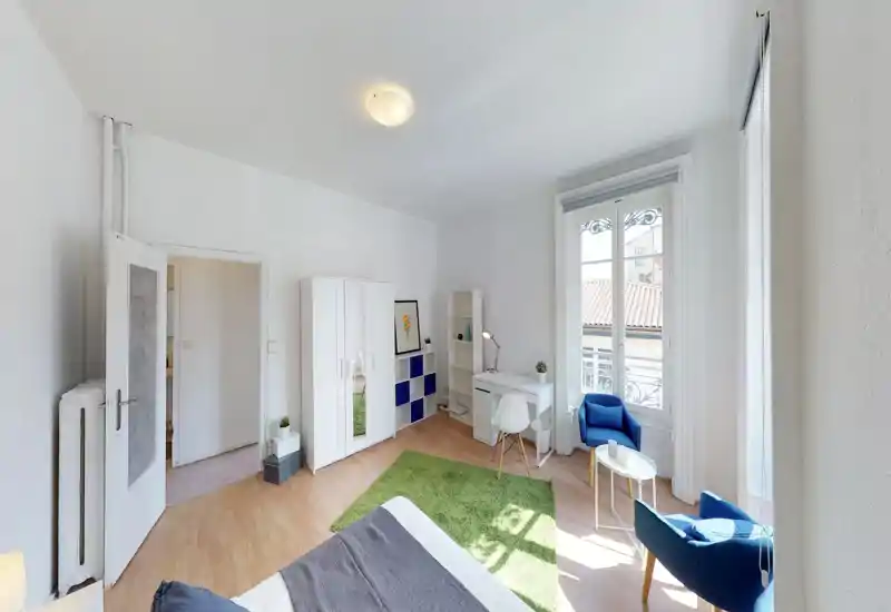 Bright, well-staged bedroom with a large window, cozy green rug and comfortable seating — ideal for short-term rentals and listings.