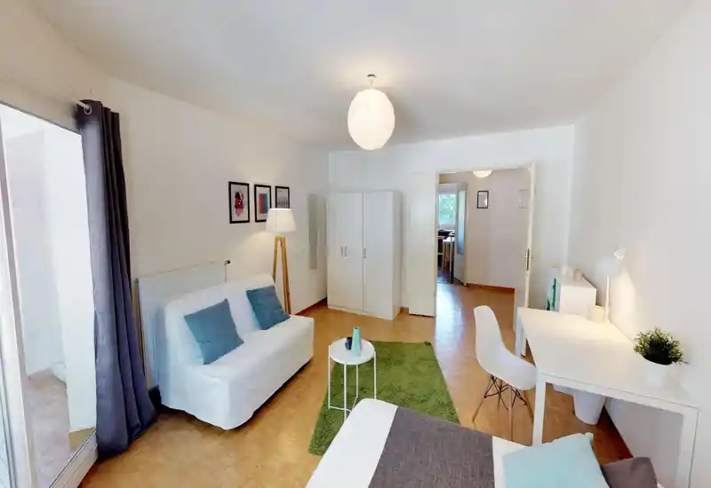 Spacious, bright bedroom with a comfortable bed in the foreground, a cozy seating area, desk, and wardrobe — ideal for working and relaxing with lots of natural light.