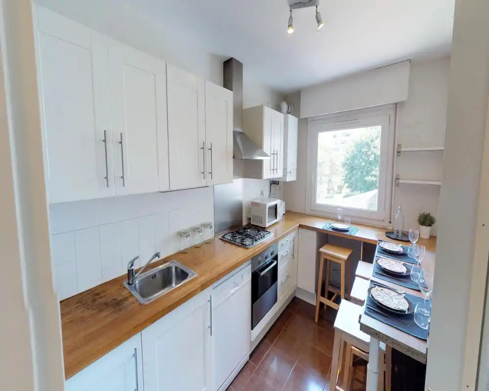 Bright, modern kitchen with white cabinets, wooden countertops, gas hob and integrated oven. A cosy breakfast bar by the window is set for dining, making this a practical and inviting cooking space.