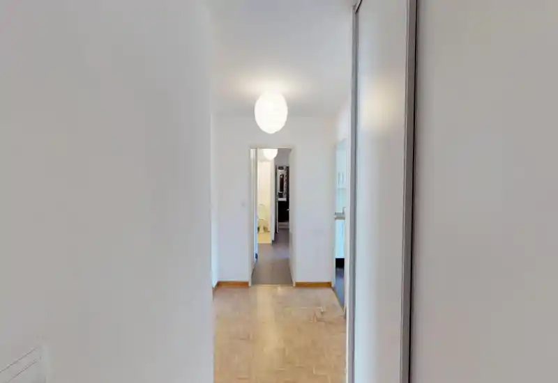 Entrée lumineuse et minimaliste avec parquet menant aux pièces adjacentes ; suspension et murs blancs pour une première impression propre et neutre.