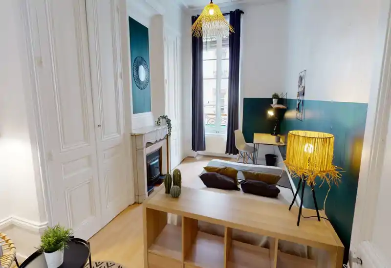 Bright, stylish bedroom with a low shelving unit behind the bed, green-accent wall and warm rattan lamps; a desk by the window provides a practical workspace.