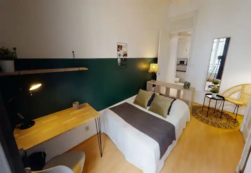 Bright, stylish bedroom with a double bed dressed in neutral linens, a dark green half-painted feature wall, small desk and cozy seating — well staged for a rental listing.