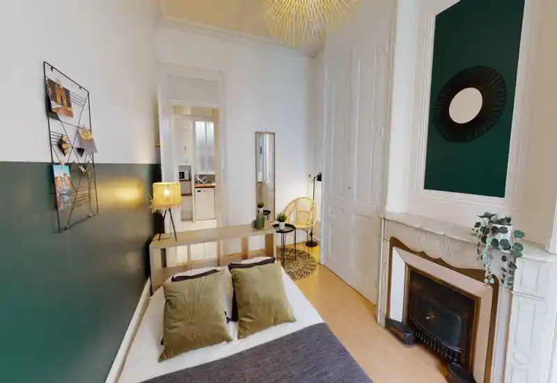 Bright, stylish bedroom with a cozy double bed, textured cushions and tasteful green-accented decor. The room features original mouldings, a decorative fireplace and a small seating nook by the wardrobe.
