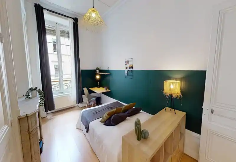 Bright, stylish bedroom with a centrally placed double bed, cozy textiles and decorative cushions, a working desk by a large window and warm ambient lighting.
