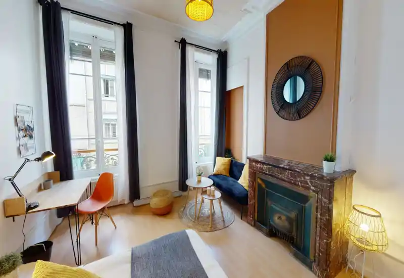 Bright, stylish bedroom with a comfortable bed in the foreground, a small seating area by the window, and an elegant marble fireplace — ideal for cosy stays.