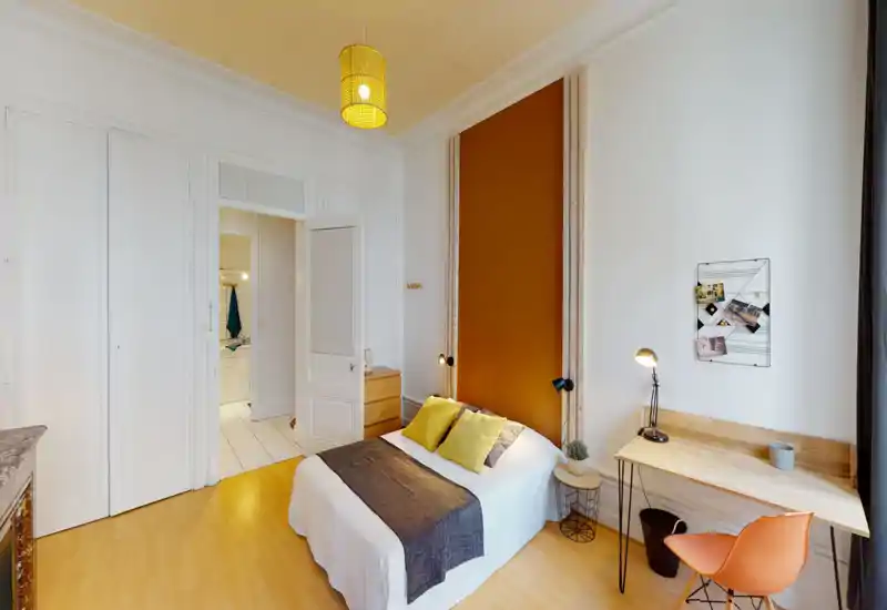 Bright, stylish bedroom with a double bed positioned against a warm accent wall, bedside lamps and a simple wooden desk by the window — a cozy, well-lit space ideal for restful stays.