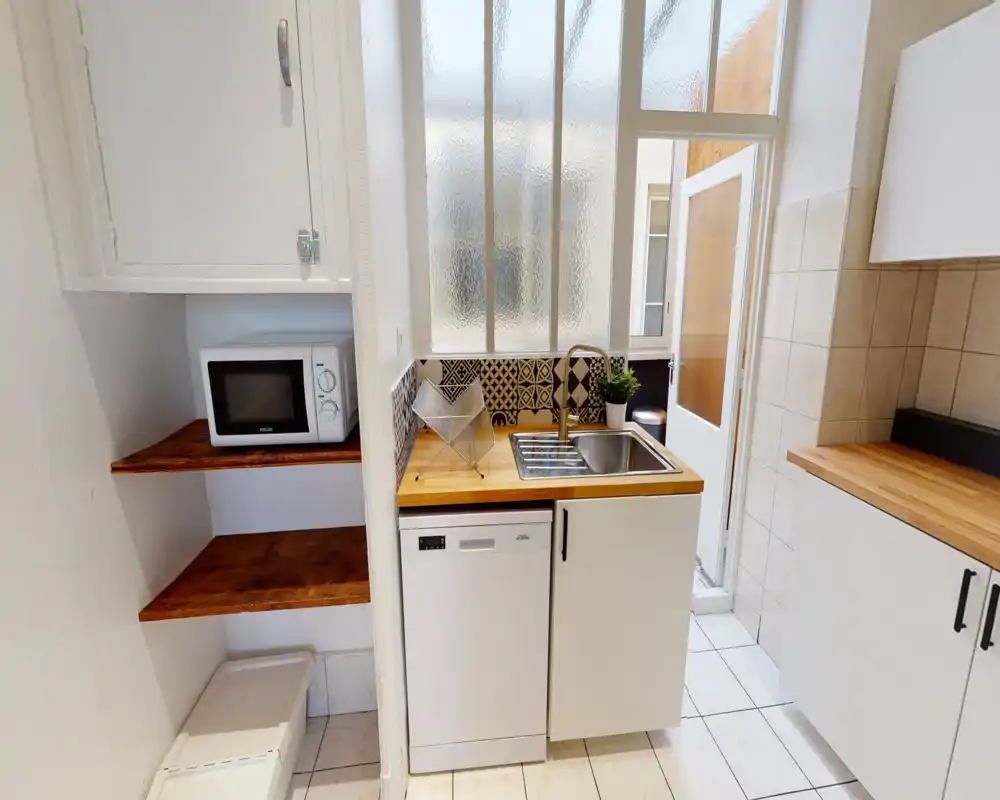 Cuisine compacte et lumineuse avec plan de travail en bois, évier inox, micro-ondes et crédence carrelée décorative — idéale pour un petit appartement.