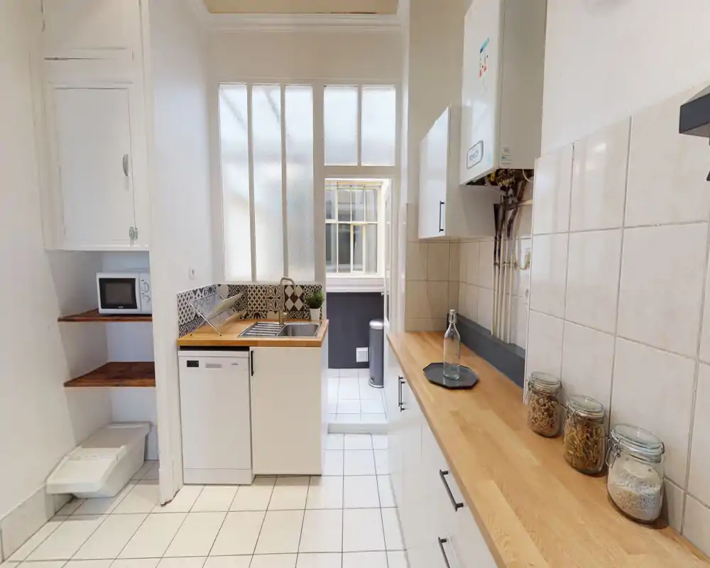 Cuisine compacte et lumineuse avec plans de travail en bois, crédence carrelée et évier intégré avec lave-vaisselle—espace propre et bien mis en valeur pour une annonce.