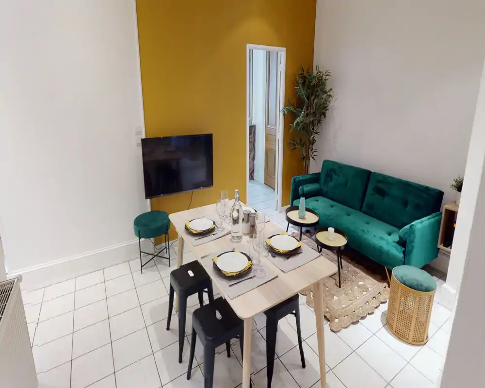 Salon lumineux et élégant avec canapé en velours vert, tabourets assortis et table à manger dressée pour quatre — mur d'accent moutarde et plantes apportent de la chaleur.