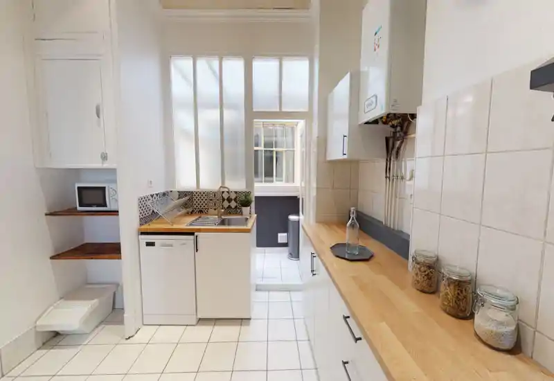 Bright compact kitchen with wooden countertops, tiled backsplash and integrated sink and dishwasher—clean, neatly styled space ideal for rental listings.