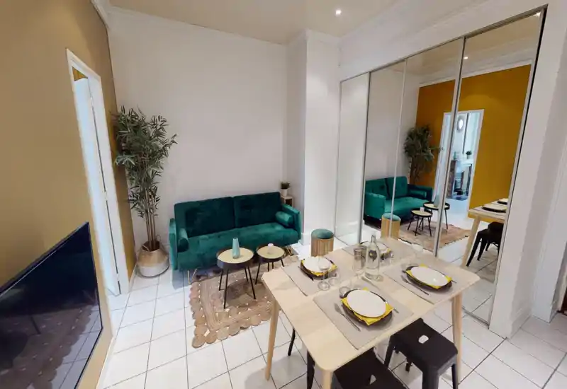 Bright, stylish living room with a green velvet sofa, coffee tables and a small dining area; mirrored wardrobe adds depth and modern character.