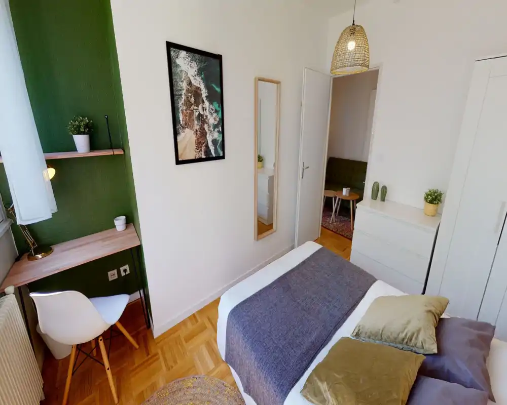 Bright, well-styled small bedroom with a cozy double bed, soft pillows and a woven pendant light; includes a compact desk by the window and white storage unit for efficient use of space.