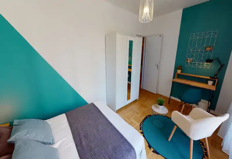 Camera da letto luminosa e moderna con un ampio letto con biancheria neutra, un armadio bianco, una piccola scrivania e una poltrona accogliente su una parete accentata turchese con tappeto coordinato.