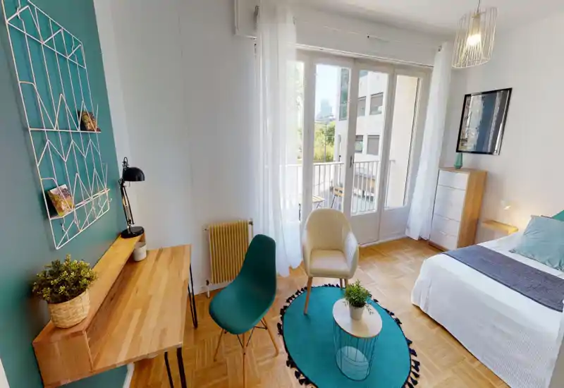 Camera da letto luminosa e accogliente con letto matrimoniale, ampie finestre francesi che garantiscono molta luce naturale e accenti turchesi coordinati tra tappeto e scrivania.