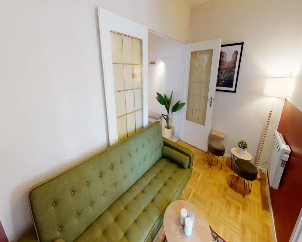 Zona giorno luminosa e ben allestita con divano verde in stile mid-century, tavolino e illuminazione accogliente — perfetta per rilassarsi.