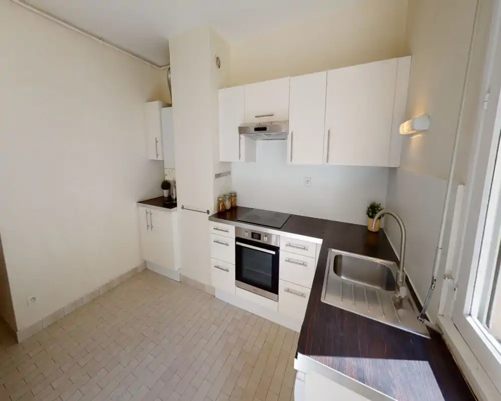 Cucina moderna e luminosa con mobili bianchi, forno incassato e piano a induzione, piani scuri effetto legno e lavello in acciaio; disposizione ordinata e funzionale con luce naturale dalla finestra.