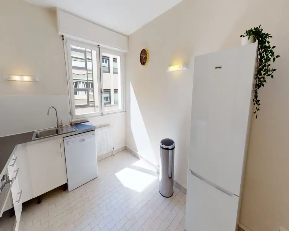 Cucina luminosa e moderna con ampia finestra, mobili bianchi, lavastoviglie e frigorifero a libera installazione; pavimento piastrellato e stile minimal.