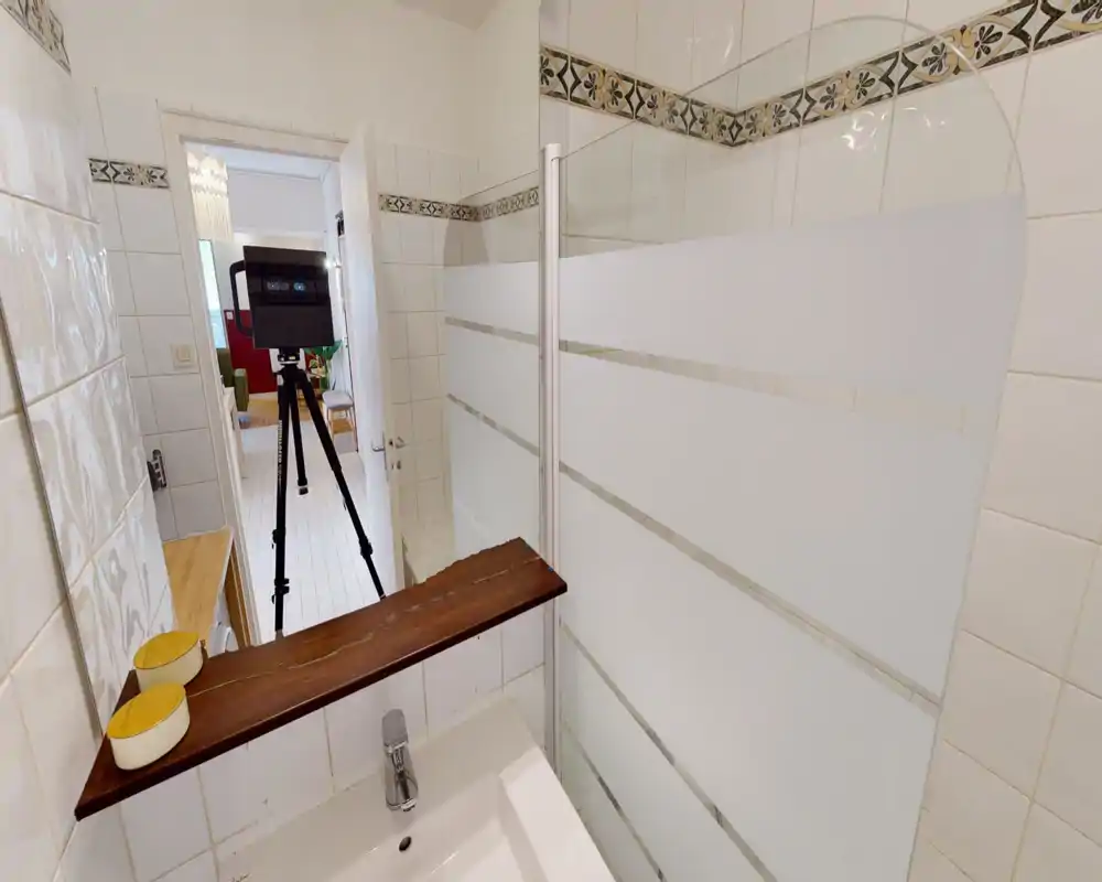 Bagno piastrellato con lavabo e parete doccia in vetro; piastrelle bianche luminose con fascia decorativa.