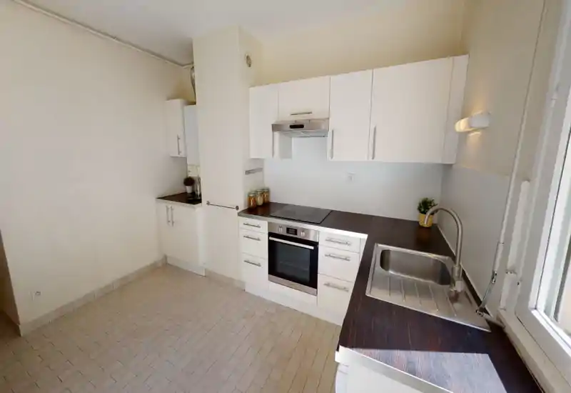Bright modern kitchen with white cabinets, a built-in oven and induction hob, dark wood-effect countertops and a stainless-steel sink; neat and functional layout with natural light from a nearby window.