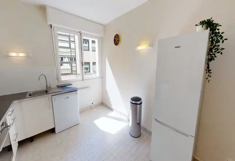 Bright, modern kitchen with a large window, white cabinets, dishwasher and freestanding fridge; clean tiled floor and minimalist styling.