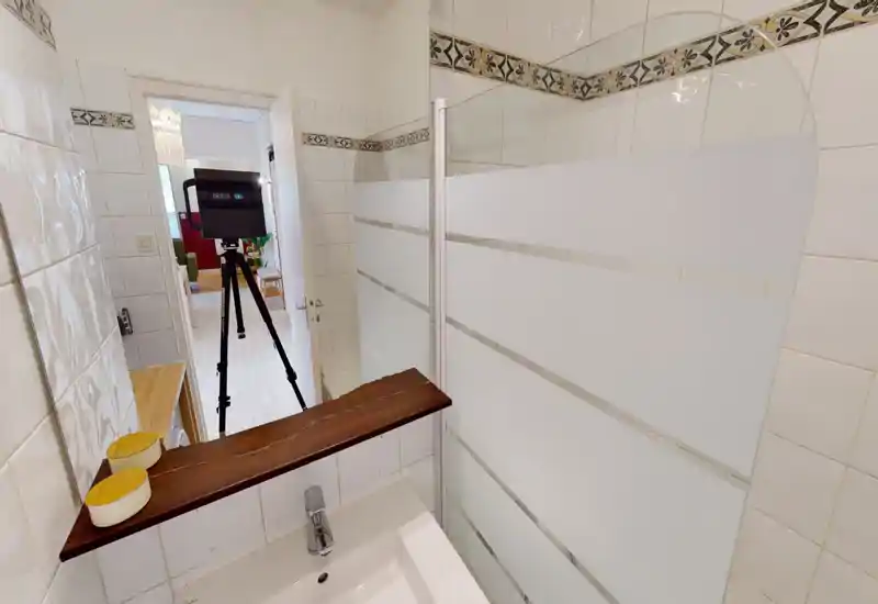 Small tiled bathroom with a sink and a glass shower screen; bright, clean white tiles and decorative border trim.