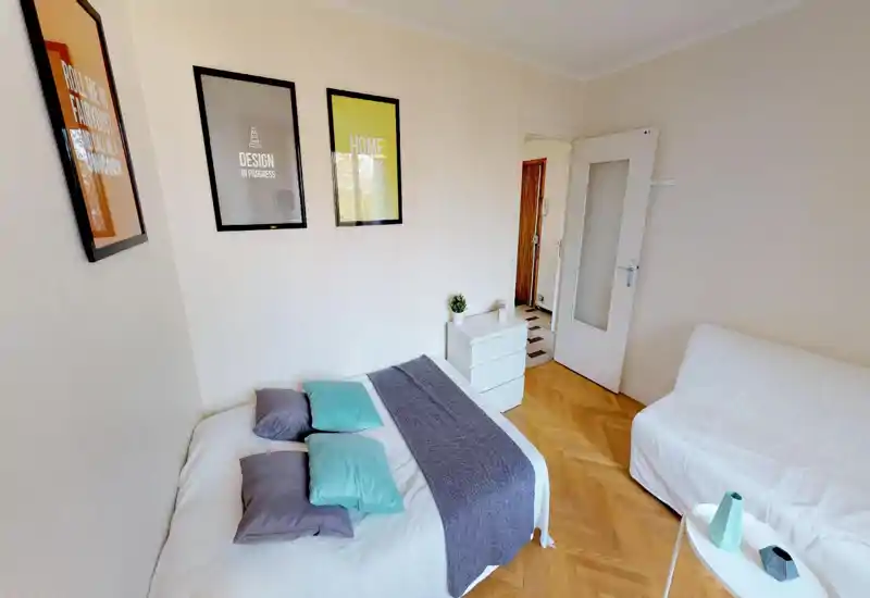 Bright, comfortably staged bedroom with a double bed dressed in neutral linens, colored pillows and a textured throw; framed wall art and a small dresser add personality.