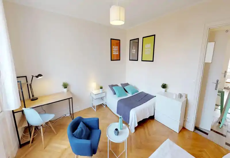 Bright, neatly staged bedroom with a double bed, bedside tables and soft textiles. The room features wooden herringbone floors, a study desk by the window and pleasant decorative accents.