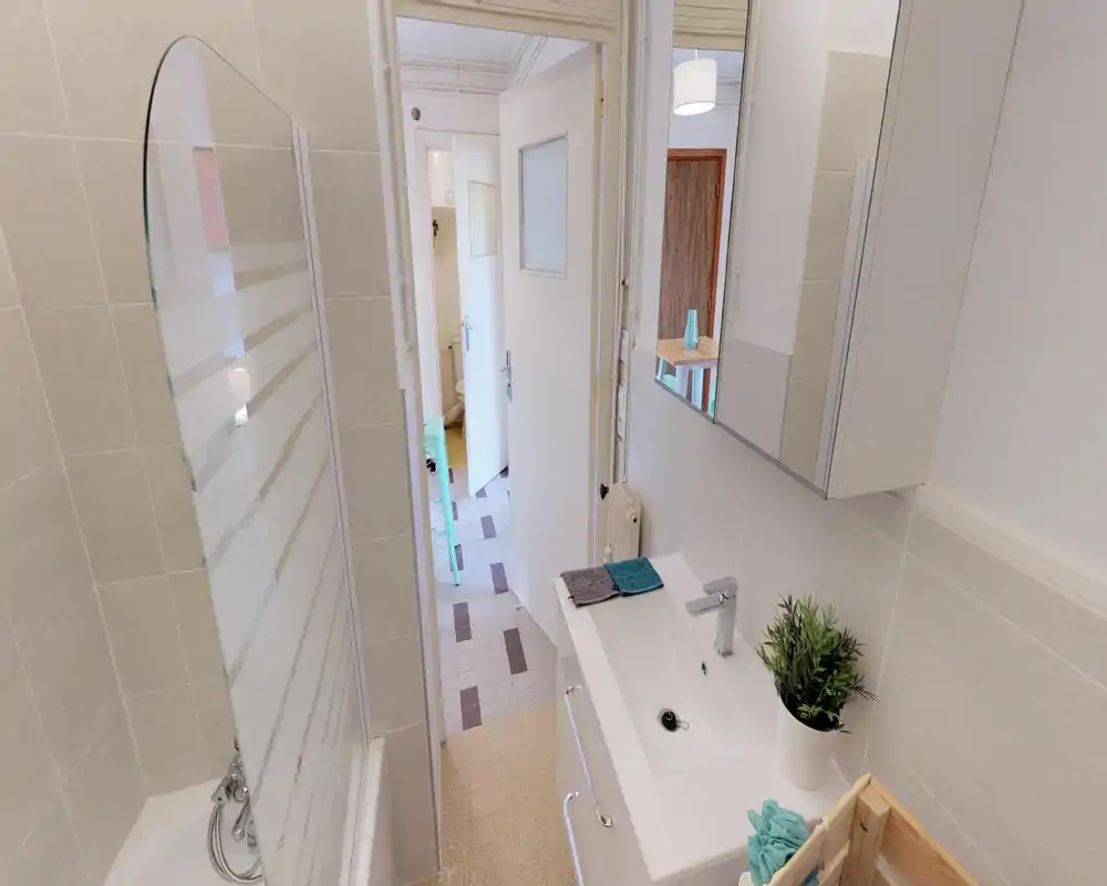 Salle de bain compacte et propre avec lavabo et armoire-miroir, baignoire avec pare-douche en verre et carrelage clair; espace lumineux et bien rangé.