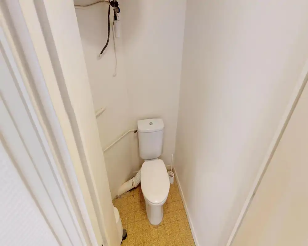 Petite salle d'eau avec WC standard, murs blancs et sol carrelé. Agencement compact adapté à un WC séparé.