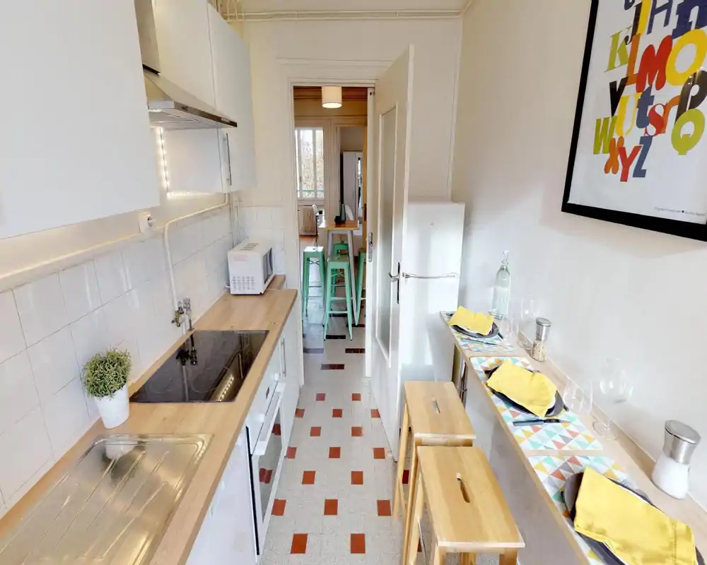 Cuisine compacte et lumineuse avec plan de travail en bois, plaque à induction, évier et petit bar avec tabourets — bien aménagée pour courts séjours.