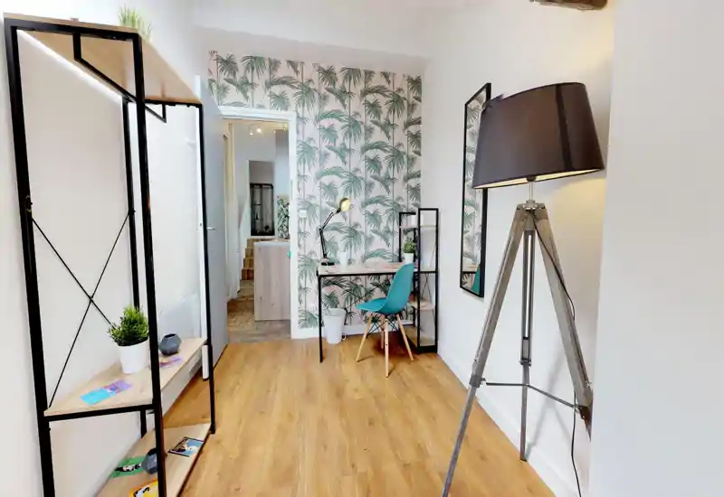 Zona giorno luminosa e curata con scrivania, carta da parati decorativa e lampada da terra a treppiede — ideale per lavorare da casa o rilassarsi.