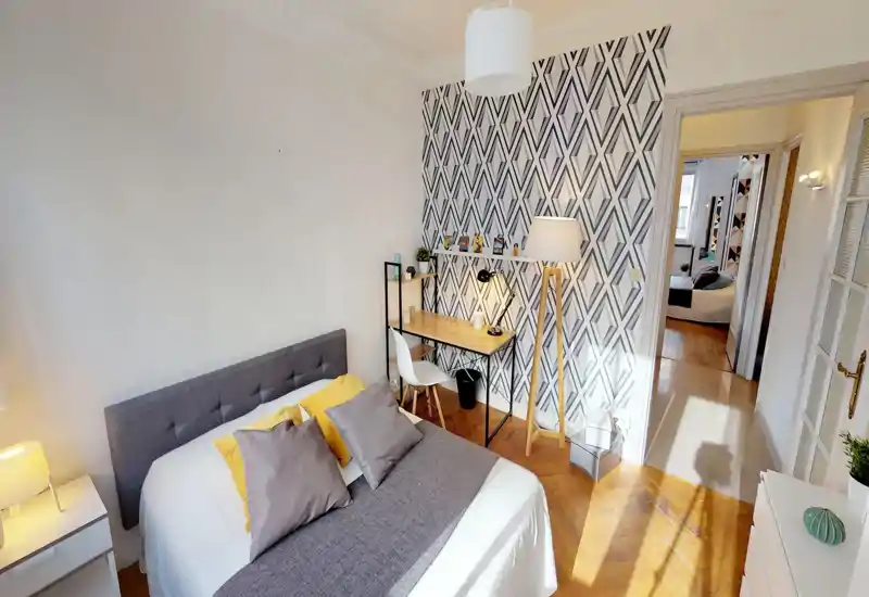 Bright, well-staged bedroom with a large bed, patterned accent wall and a small desk area — ideal for rental listings highlighting comfort and style.