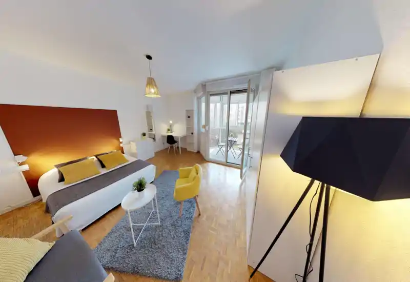 Bright, well-staged bedroom with a large double bed, cozy textiles and a sitting area. Natural light floods the room through glass doors leading to a small balcony.