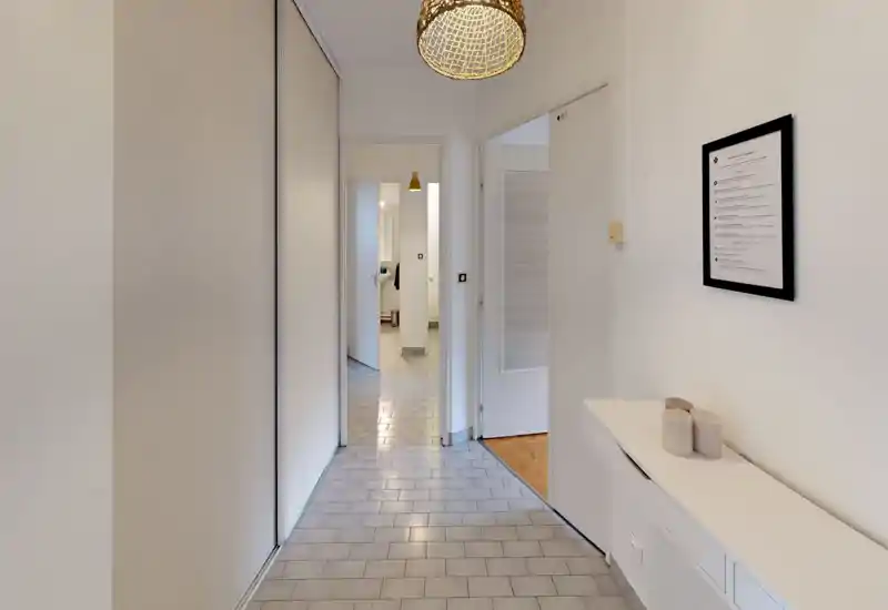 Bright, minimal entrance hallway with tiled floor, built-in storage on the left and a slim console on the right; leads to adjacent rooms and bathroom.
