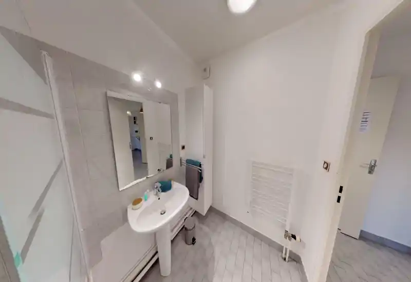 Clean, modern bathroom with a pedestal sink, large mirror, towel radiator and a tall storage cabinet. Neutral tiles and bright white walls create a fresh, minimalist feel.
