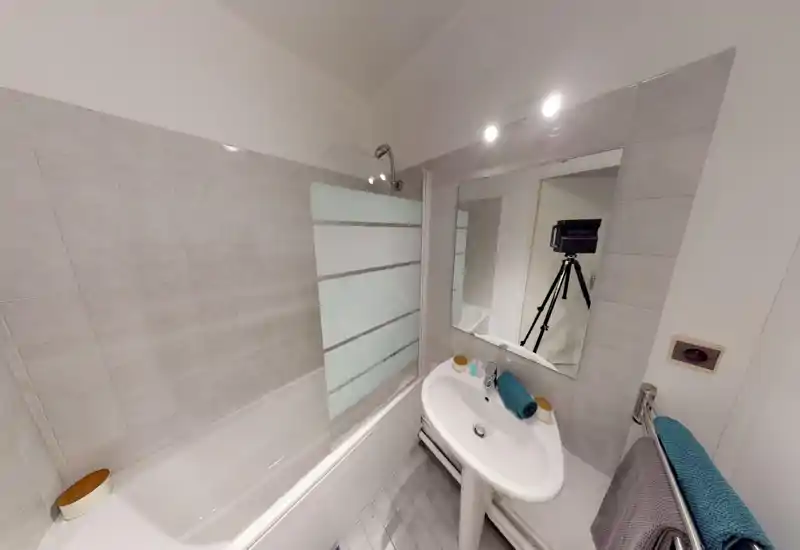 Clean, compact bathroom with a bathtub/shower combination, pedestal sink, large mirror and tiled walls. Good lighting and modern fixtures make it practical for short stays.
