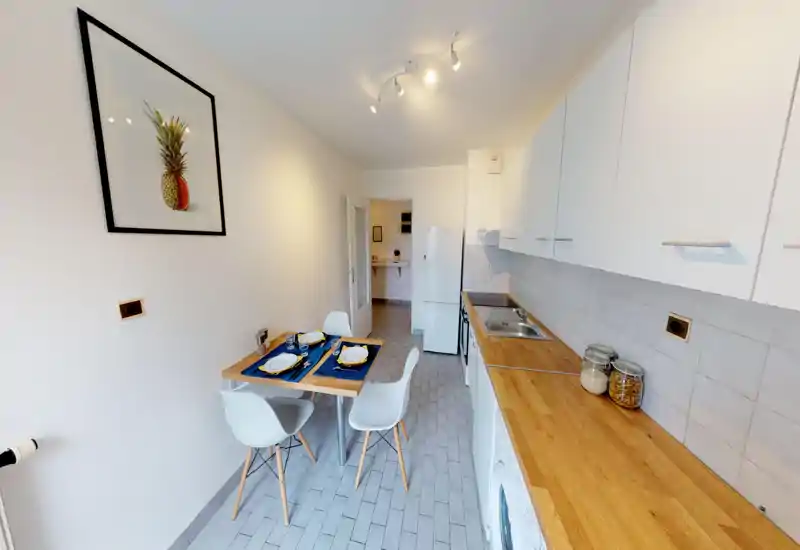 Bright, modern galley kitchen with wooden countertops, white cabinets and a small set dining table for two. Clean, tidy styling with jars and simple decor.
