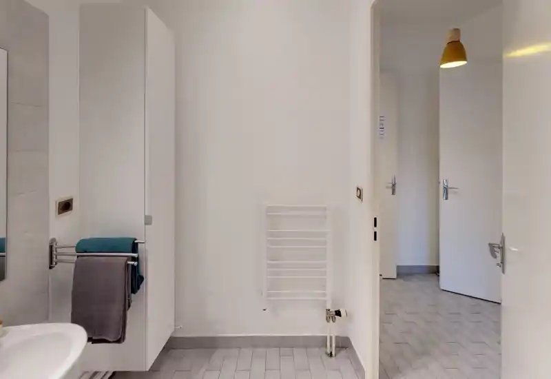 Clean, minimal bathroom view with a towel rail, cabinet and sink; neutral tiles and bright, even lighting.