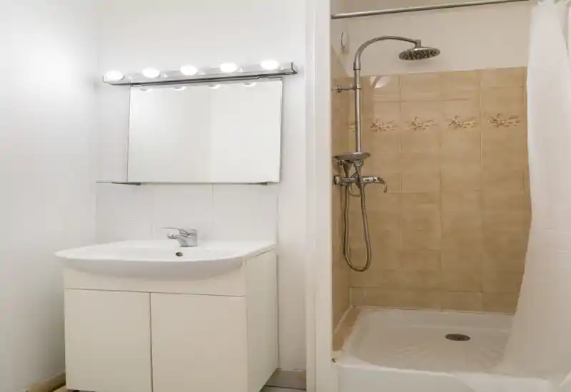 Bagno compatto e pulito con lavabo, specchio illuminato e doccia piastrellata con soffione a pioggia. Piastrelle dai toni neutri e buona illuminazione lo rendono pratico.