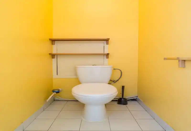 Piccolo WC con water in ceramica bianca, mensole in legno e pareti giallo brillante che creano un'atmosfera calda e ordinata.