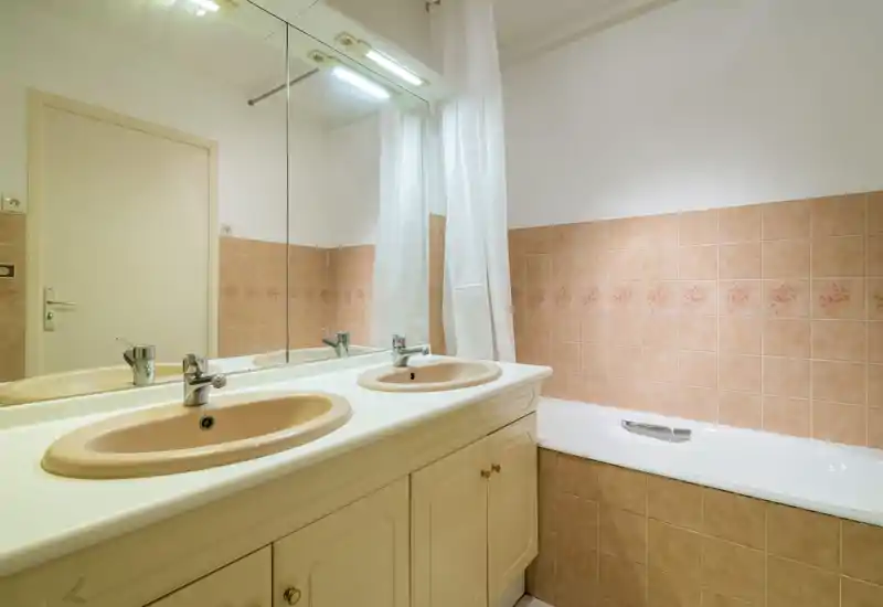 Bagno luminoso e ben tenuto con mobile lavabo doppio, grande specchio e vasca con piastrelle in tonalità beige calde.