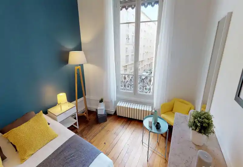 Camera da letto luminosa e di stile con una parete accent color turchese, letto con cuscino giallo, lampade da comodino e una grande finestra che illumina la stanza.
