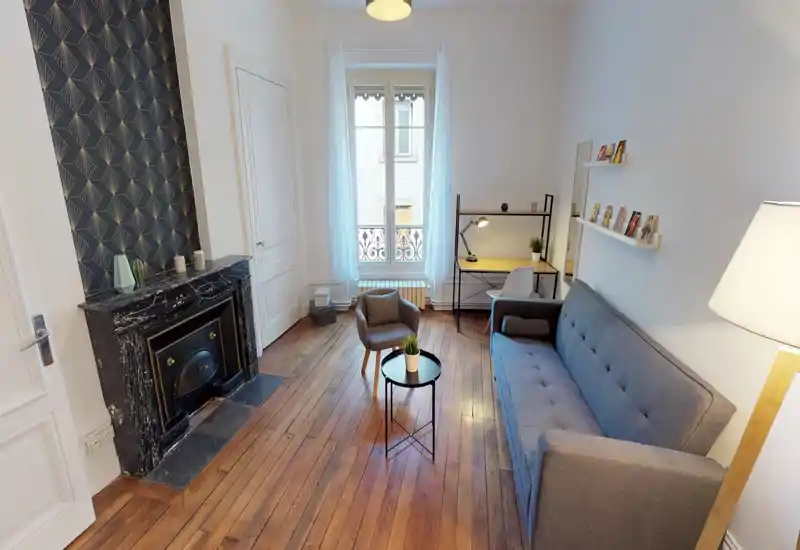 Bright, stylish living room with a comfortable grey sofa, armchair and a small coffee table. Large window provides natural light and a compact desk area offers a practical workspace.