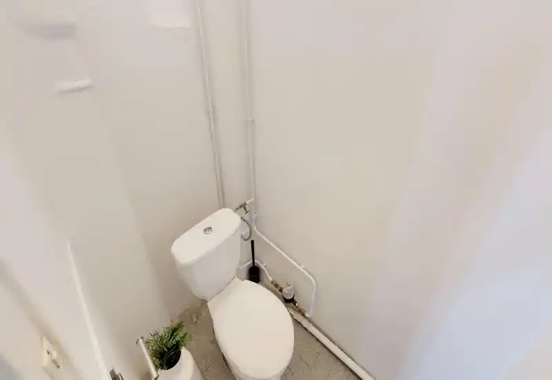 Toilettes compactes et propres avec plomberie apparente et murs blancs neutres — petite salle d'eau adaptée aux invités.