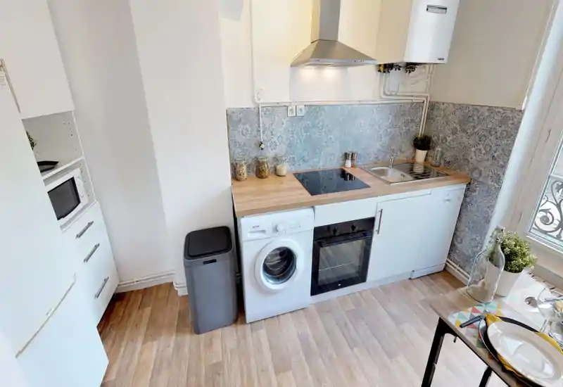 Cuisine compacte et lumineuse avec plan de travail imitation bois, plaque à induction, four encastré et évier. Crédence à motifs et petites plantes décoratives apportent une ambiance moderne et chaleureuse.