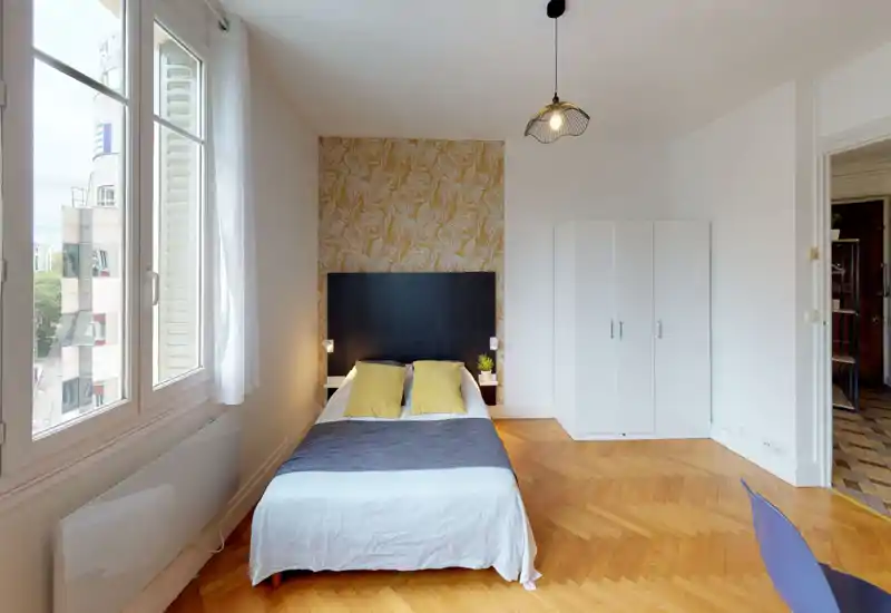 Sunny, stylish bedroom with a double bed, decorative wallpaper and parquet floors; large window provides abundant natural light.