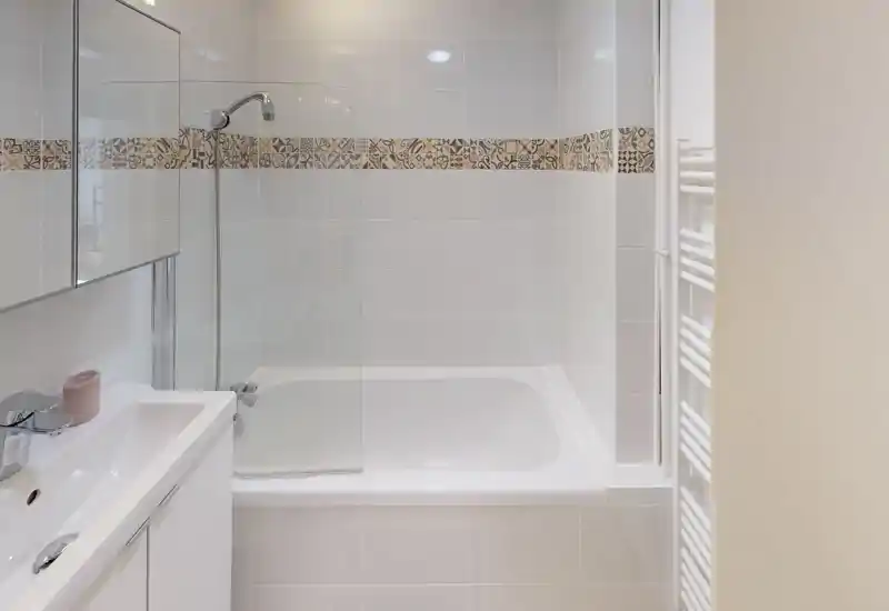Clean, well-lit bathroom with a bathtub and wall-mounted shower head, white tiles and decorative tile border for a modern look.