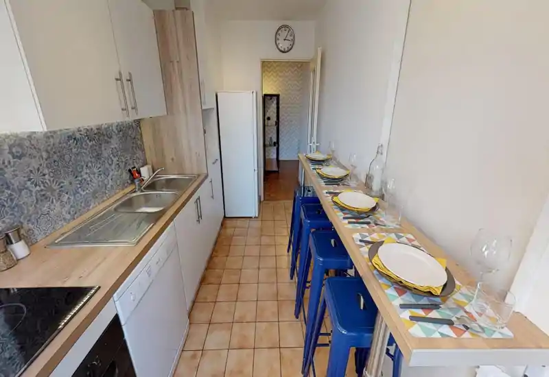 Long galley kitchen with patterned backsplash, double sink, appliances and a breakfast bar with blue stools set for dining; bright and well organized.